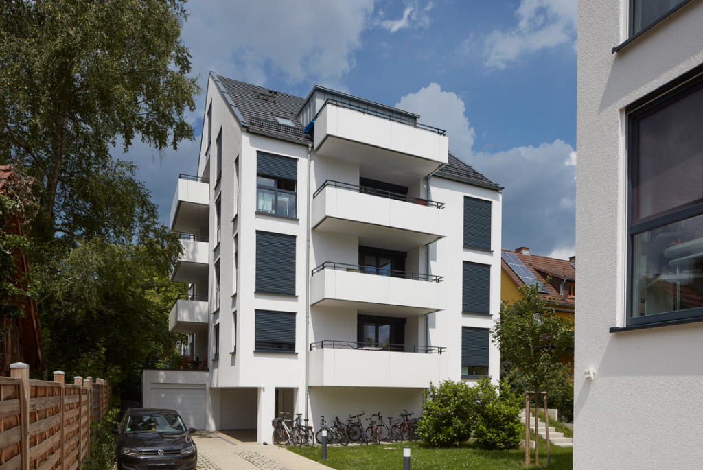 Modernes Mehrfamilienhaus mit Balkonen und weißer Fassade.